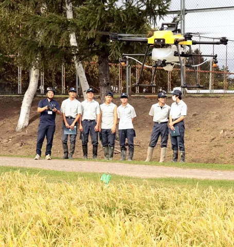 農薬散布用ドローンのデモ飛行を見学する岩見沢農業高の生徒らの写真