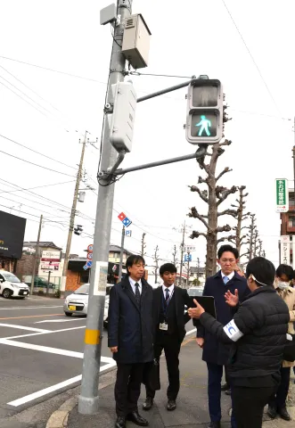 実証視察会で、交差点に設置された通信機器などについて説明を受ける川崎ひでと総務大臣政務官（左から３人目）